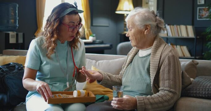 Senior woman grandmother receives a daily dose full palm of pills from a caregiver to drink, feels good and satisfied receiving health care at home. 
