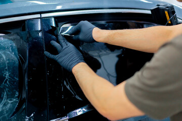 close-up repairman smooths the protective film for tinting on the car glass with a scraper detailing