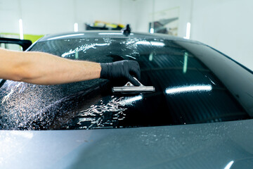 close-up repairman smooths the protective film for tinting on the car glass with a scraper detailing