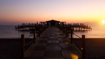 Fototapeta premium Early dark morning over the sea, the pier is barely lit by the first rays of the sun and electric lamps.