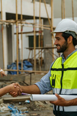 Foreman man with Yellow helmet holding plan roll shaking hand with someone in constuction site