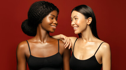 Multi Ethnic Group of beauty Womans with diffrent types of skin  together and looking on camera. Two Diverse ethnicity women -  African and Asian posing and smiling against red background.
