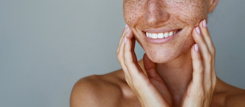 Skin care. Freckles. Cropped portrait of a young woman  is posing with a chin look against grey background. Natural beauty and glowing clean hydrated skin
