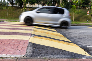 Car slowing down at speed bump or road hump painted in yellow and black stripe. Motion blur intended.