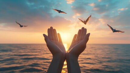 Hands open palm up worship with birds flying over calm water sunset background. Concept of praying for blessing from God.