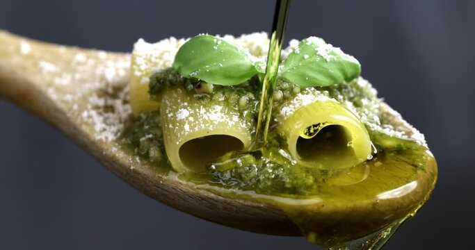 Super slow motion macro of fresh organic olive oil dripping on traditional italian dish of pasta with pesto Genovese sauce with grated parmesan cheese in wooden spoon on soft background at 1000 fps.
