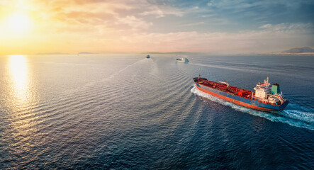 A group of cargo bulk ships and chemical goods or oil tanker sailing with speed over the ocean into the sunset - 723886033