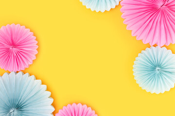 Frame made of tissue paper fans in a blue and pink colors on a yellow background. Festive...
