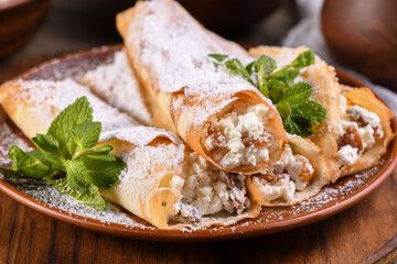 Thin pancakes filled with cottage cheese, honey and raisins, rolled in the form of a tube, sprinkled with powdered sugar, garnished with mint. Festive dish for the pagan Slavic holiday Maslenitsa - obrazy, fototapety, plakaty