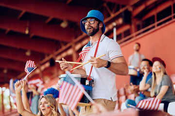 Happy sports fan cheering for USA while playing drums at stadium stands.