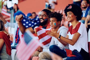 Happy black family cheering for USA during sports match at stadium.