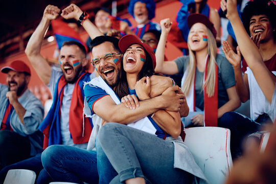Group of cheerful sports fans celebrating victory of their favorite team while spectating game from stadium stands.