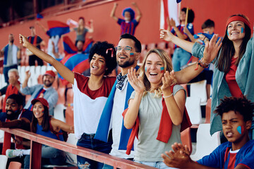 Group of happy friends cheering from stadium stands during sports match.