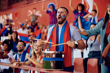 Passionate sports fan playing drums during match at stadium.
