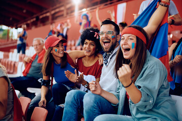 Multiracial group of happy friends cheering while watching sports game at stadium. - obrazy, fototapety, plakaty