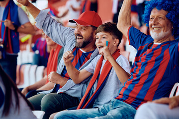 Happy boy cheering with his father and grandfather during sports match at stadium.