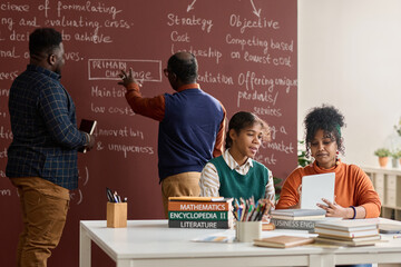Group of Black young people studying in college with two girls using tablet in foreground copy space