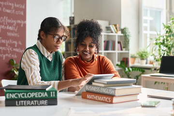 Portrait of two young Black girls using digital tablet in school classroom and working on online...