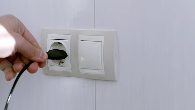 Man plugging in power cord into wall socket	