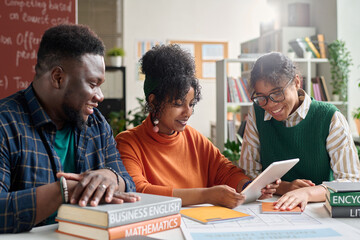 Group of African American young people studying together in college classroom and dusing digital...