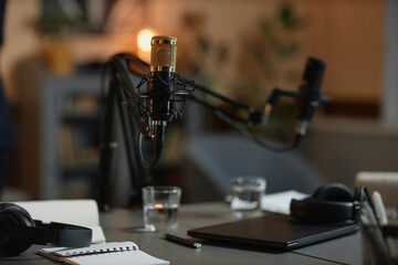 Part of podcast studio with selective focus on gold-colored professional microphone set up on desk...