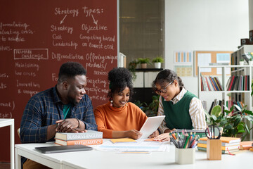 Group of three African American teenagers enjoying work together in college classroom and using...