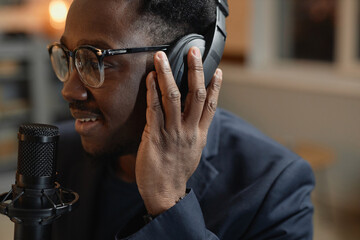 Close up view of smiling African American man wearing glasses adjusting headphones while recording...