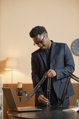 Vertical shot of African American man in black suit and eyeglasses setting microphone on flexible...