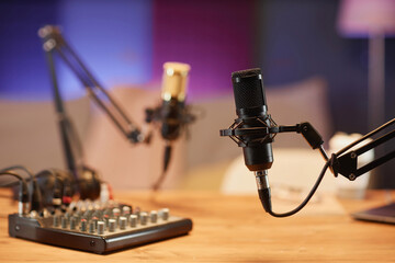 Medium shot with selective focus on black professional microphone and sound mixer on table in podcast room