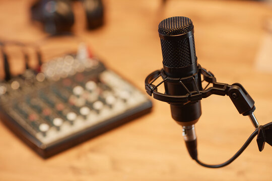 Close up shot of black condenser microphone in holder with defocused audio mixer board in studio room