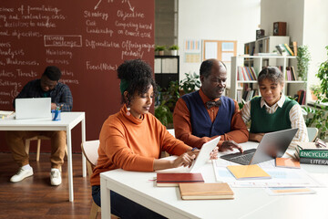 College classroom set with African American girls working with senior professor in foreground and using devices copy space - obrazy, fototapety, plakaty