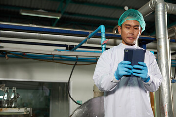 worker working on tablet beside large industrial pot in the beverage factory