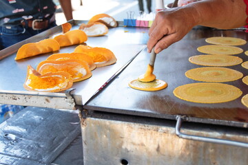 A vendor is applying flour to an iron pan to make “Thai Crispy Pancake or Kanom Buang. A...