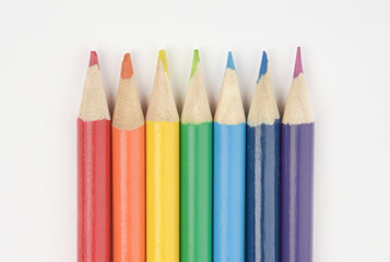A set of wooden pencils in colours of the rainbow.  Red, orange, yellow, green, blue, indigo, and violet. Arranged in a line on white background. Close Up.