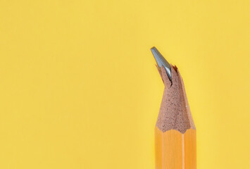 Broken or damaged wooden pencil tip or graphite on yellow background with copy space