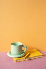 Notebook and colored pencil, coffee cup on pink desk. orange wall background. workspace