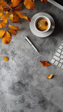 A cup of coffee, a pen, and fallen leaves on a concrete table