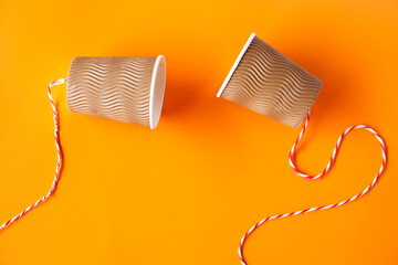 Two paper cups tied with rope for making telephone toy. Orange background. Concept, telephone toys...