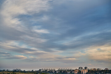 Feather clouds in the evening light on the blue sky over the fields and houses 