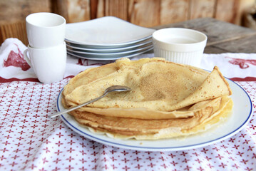traditional french homemade pancakes  in a plate served on a table with sugar on red and white tablecloth