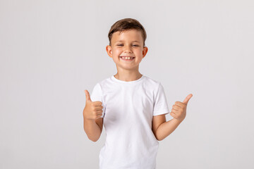 Happy smiling satisfied caucasian boy shows thumbs up looking at camera, portrait. attractive smiling boy in white casual shirt posing on white background. childhood, human emotions, lifestyle