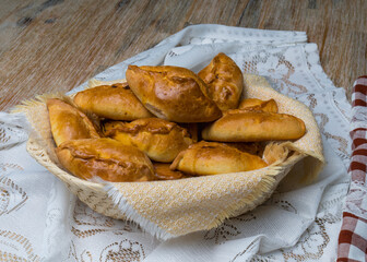 Pies with filling in a wicker basket on a wooden table. Country motive.