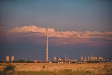 Fototapeta na wymiar Oil refinery seen on the horizon on the wheat field at sunset. Polluting industry in the environment