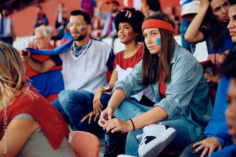 Wall mural Displeased young woman and her friends watching sports match at stadium. - Wall murals