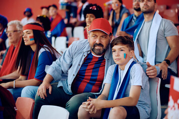 Sports fan and his son watching match from stadium stands.