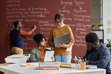 Team of African American college students doing group study in college classroom with blackboard in...