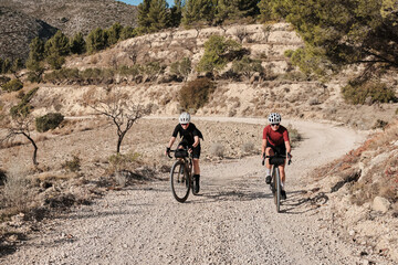 Two professional women cyclists riding gravel bicycles on a gravel road on a sunny summer day....