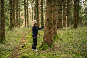 middle-aged white woman with brown hair, wearing a black sweater and a beige hat, in an Irish winter forest.