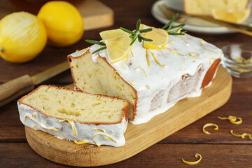 Tasty lemon cake with glaze and citrus fruits on wooden table, closeup