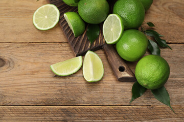 Fresh limes and green leaves on wooden table, above view. Space for text